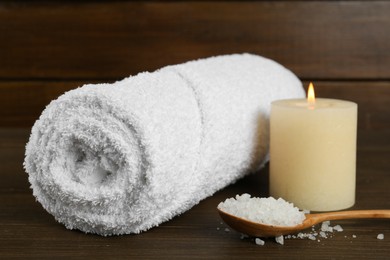 Photo of Spa composition. Towel, burning candle and spoon with sea salt on wooden table, closeup