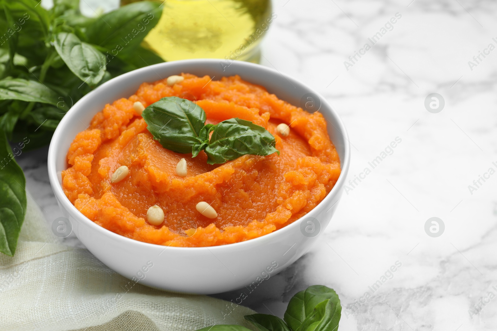 Photo of Tasty mashed sweet potato with basil and seeds in bowl on white marble table, closeup