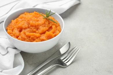 Photo of Tasty mashed sweet potato with rosemary in bowl served on grey textured table, closeup. Space for text