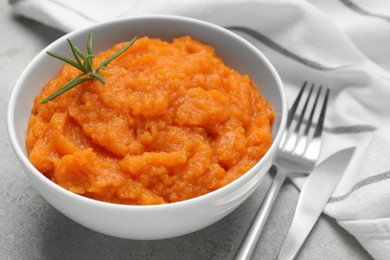 Photo of Tasty mashed sweet potato with rosemary in bowl served on grey textured table, closeup