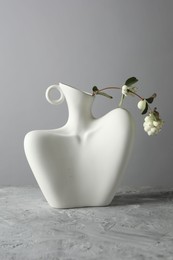 Stylish vase with snowberry branch on grey table