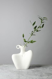 Stylish vase with green branch on grey table