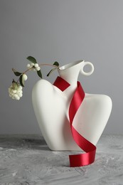 Stylish vase with snowberry branch and red ribbon on grey table