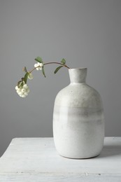 Stylish vase with snowberry branch on white table