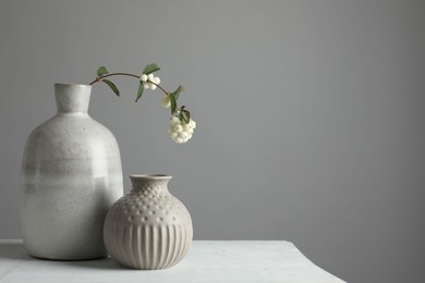 Stylish vases and snowberry branch on white table, space for text