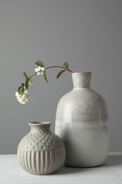 Photo of Stylish vases and snowberry branch on white table