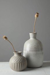 Stylish vases with dry poppy heads on white table