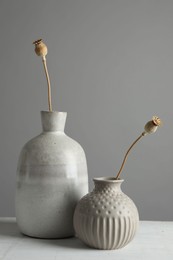 Stylish vases with dry poppy heads on white table