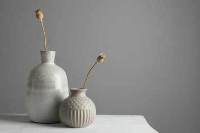 Stylish vases with dry poppy heads on white table. Space for text