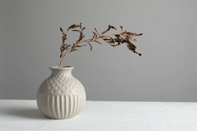 Stylish vase with dry branch on white table