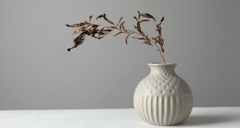 Stylish vase with dry branch on white table