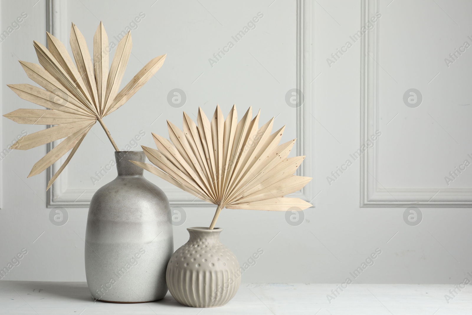 Photo of Stylish vases with dry palm leaves on white table, space for text