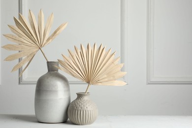 Photo of Stylish vases with dry palm leaves on white table, space for text