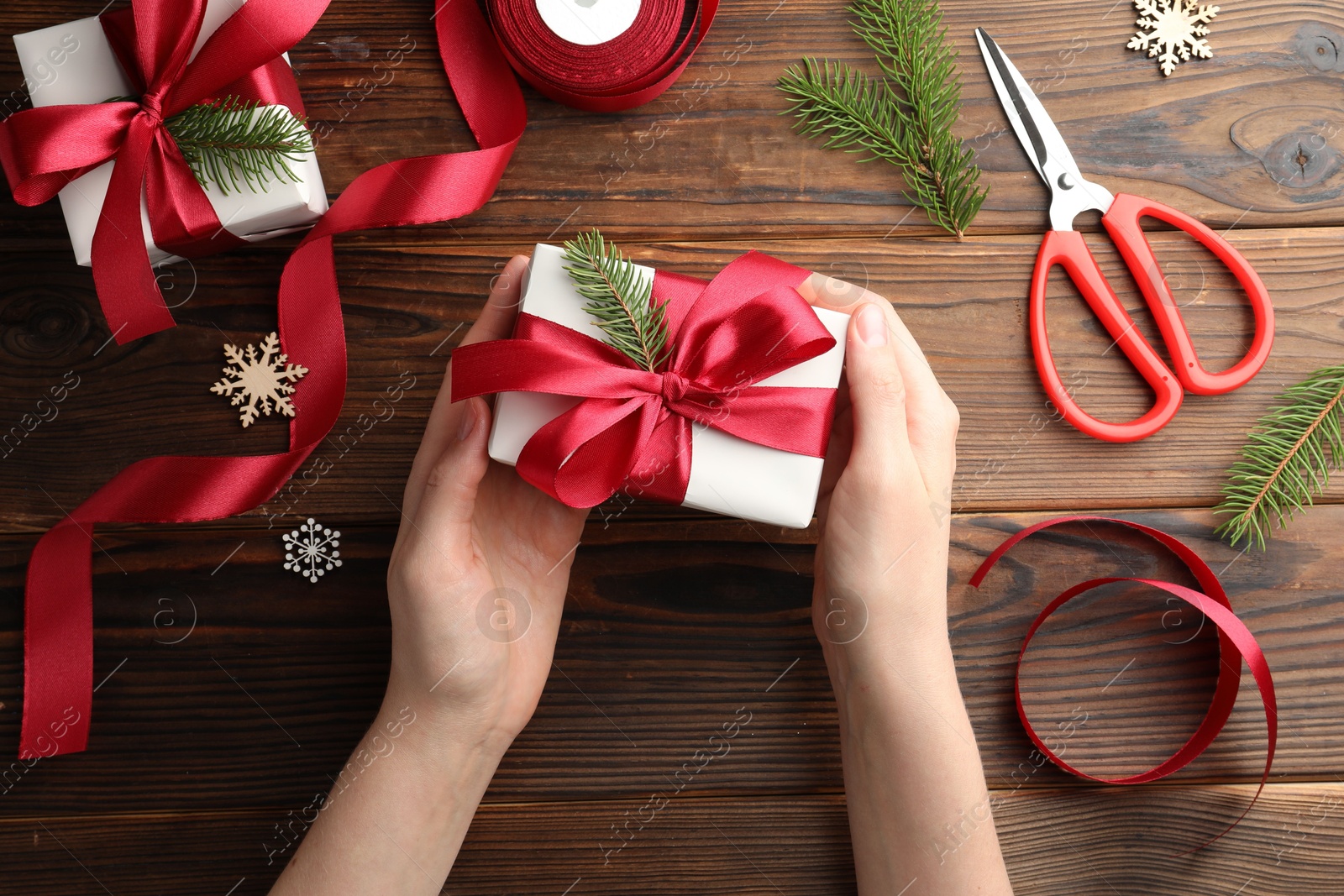 Photo of Woman holding gift box with red bow on wooden table, top view