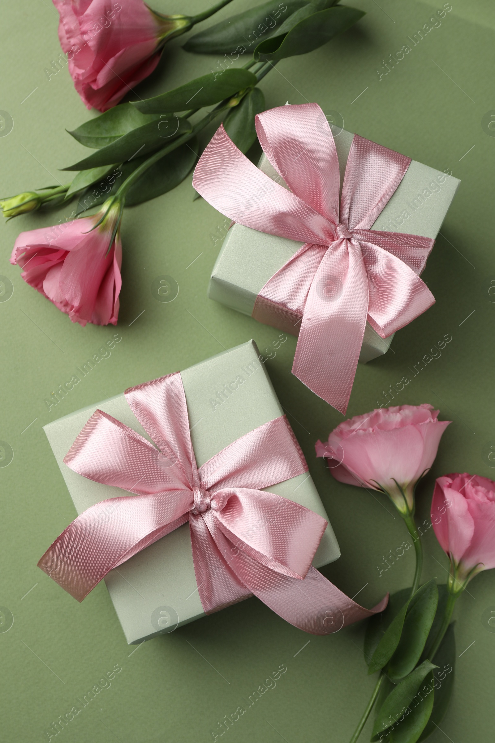 Photo of Gift boxes with pink bows and beautiful flowers on green background, flat lay