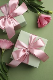 Photo of Gift boxes with pink bows and beautiful flowers on green background, flat lay