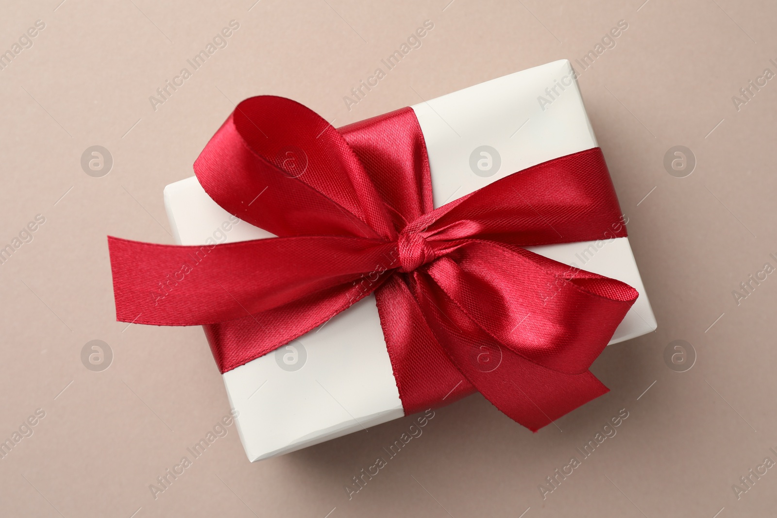 Photo of Gift box with red bow on beige background, top view