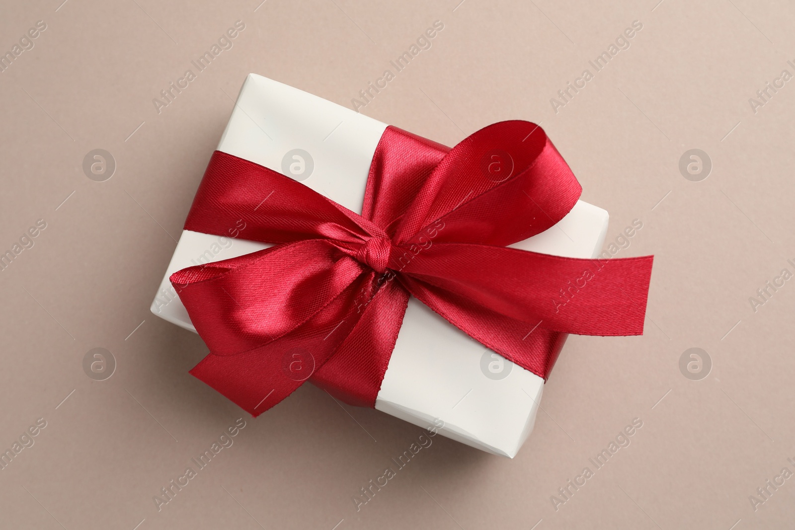 Photo of Gift box with red bow on beige background, top view