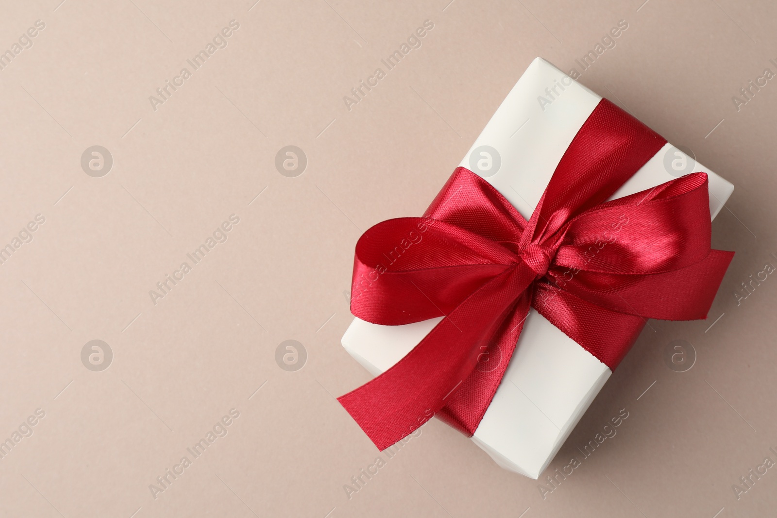 Photo of Gift box with red bow on beige background, top view. Space for text