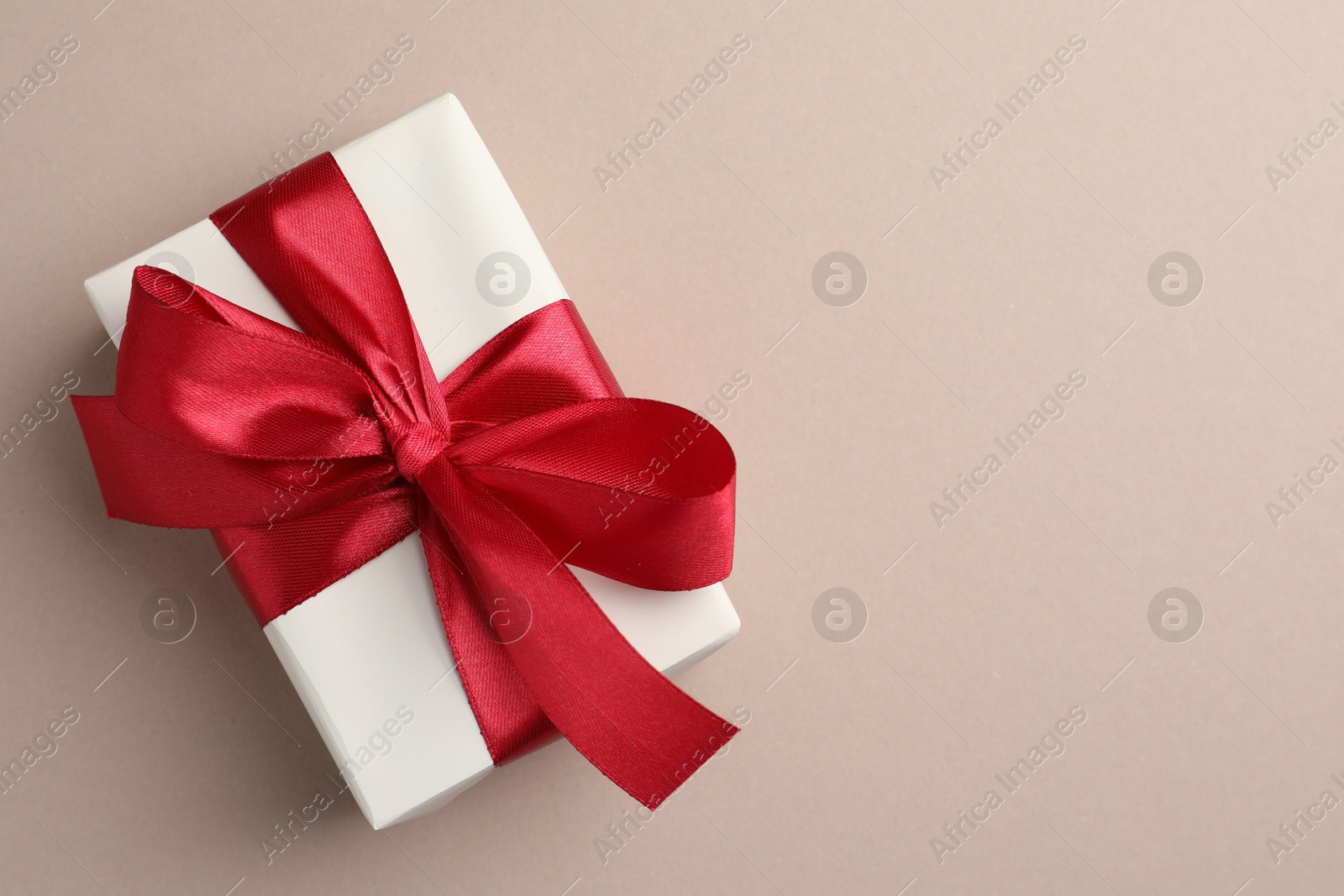 Photo of Gift box with red bow on beige background, top view. Space for text