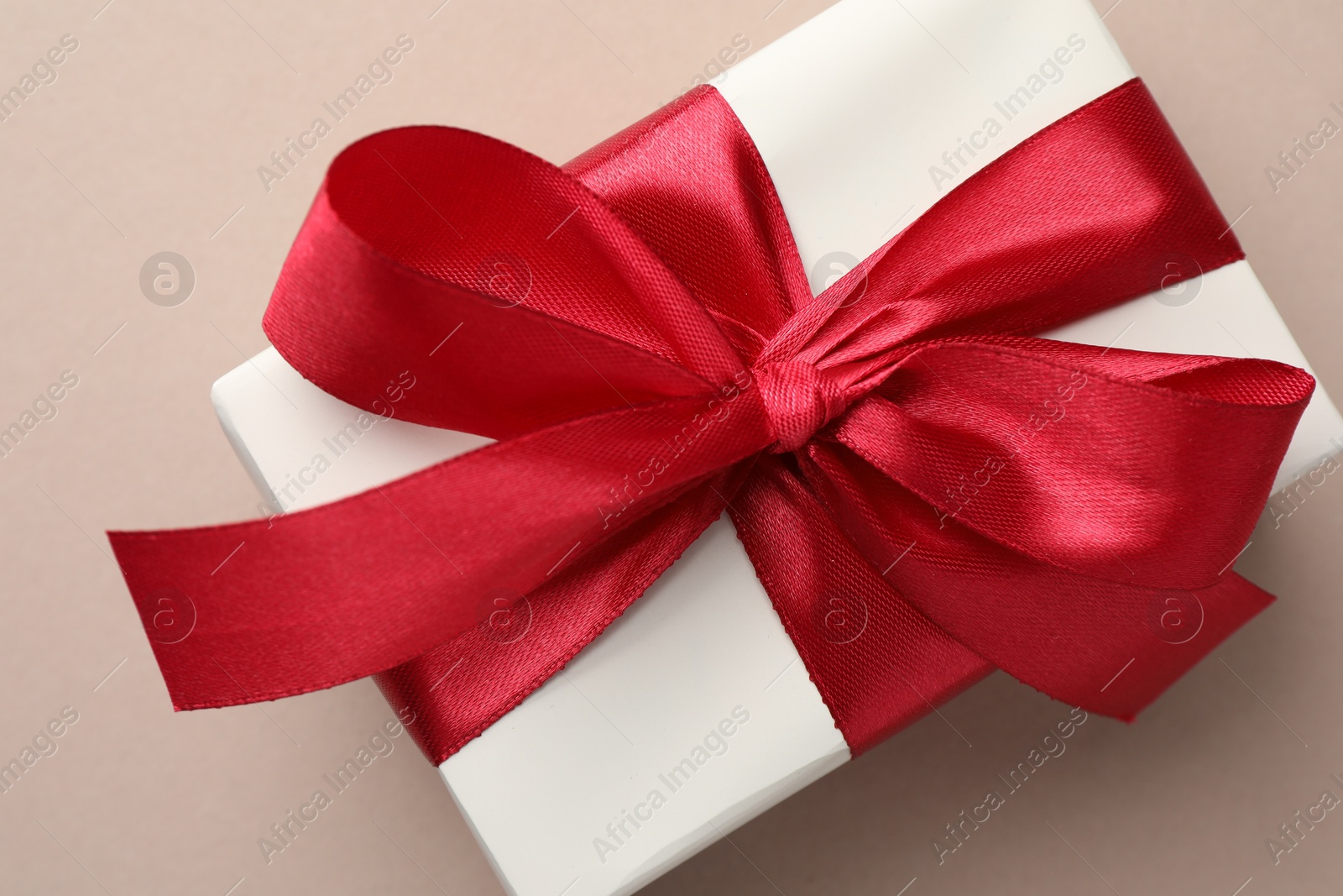 Photo of Gift box with red bow on beige background, top view