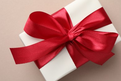 Photo of Gift box with red bow on beige background, top view