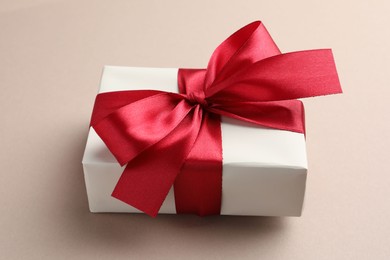 Photo of Gift box with red bow on beige background, closeup