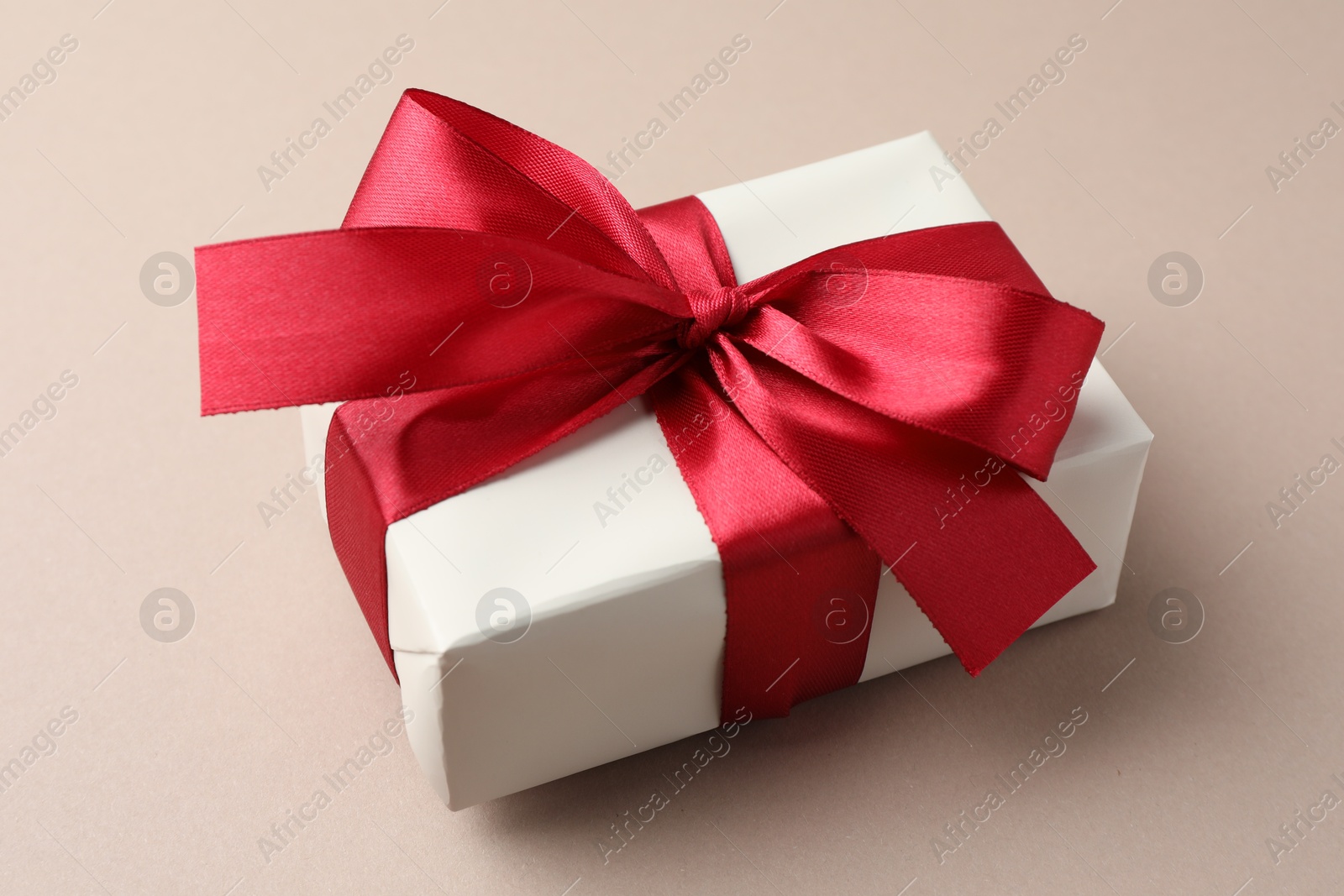 Photo of Gift box with red bow on beige background, closeup