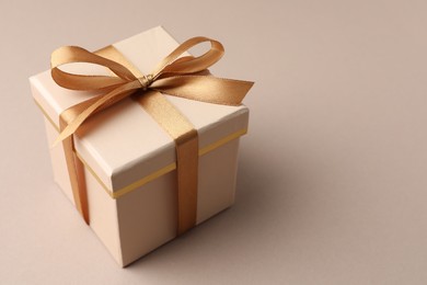 Photo of Gift box with golden bow on beige background, closeup. Space for text