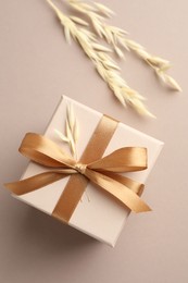 Photo of Gift box with golden bow and spikes on beige background, flat lay