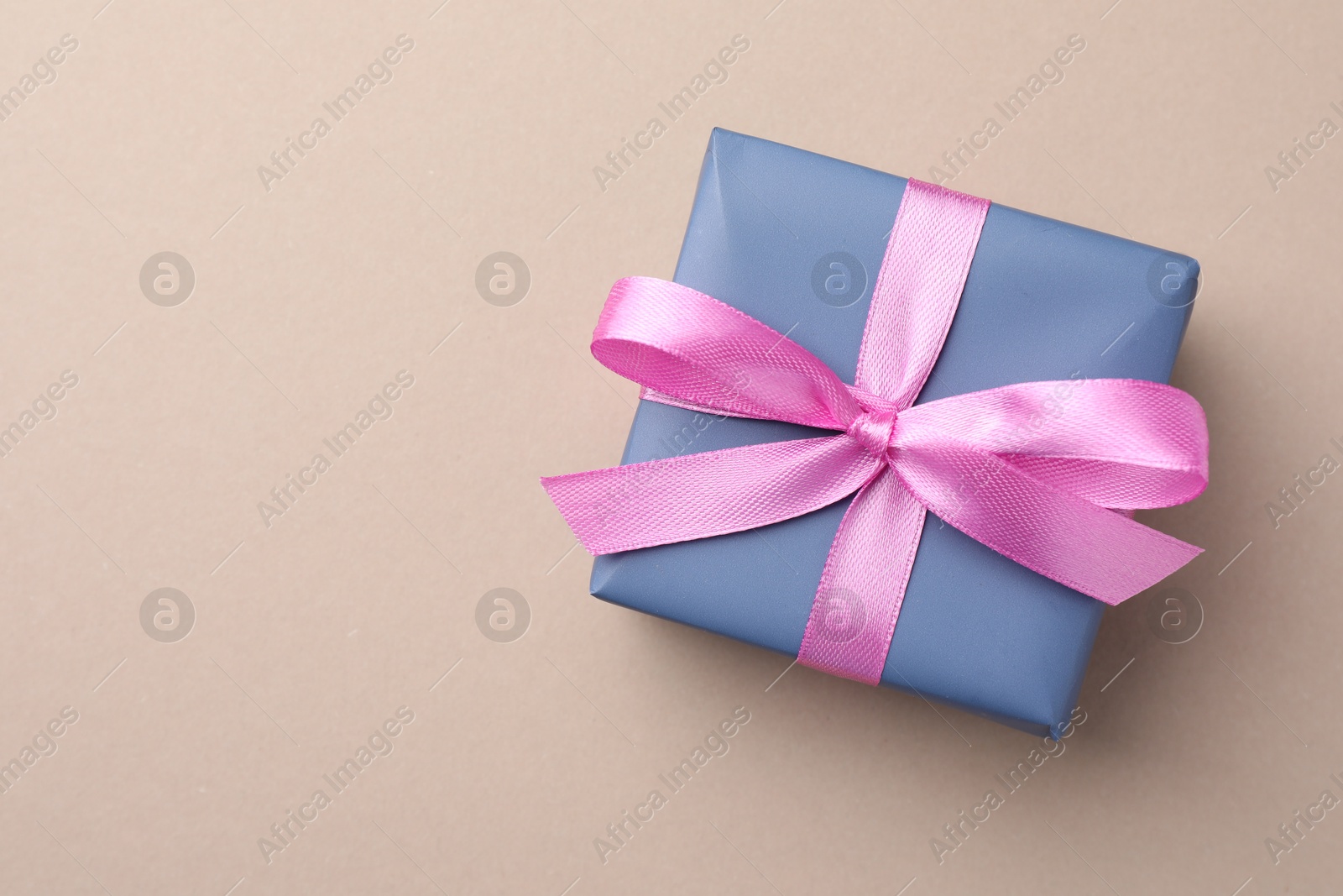 Photo of Gift box with pink bow on beige background, top view. Space for text