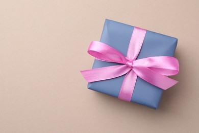 Gift box with pink bow on beige background, top view. Space for text