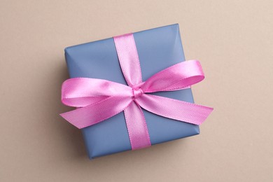 Gift box with pink bow on beige background, top view