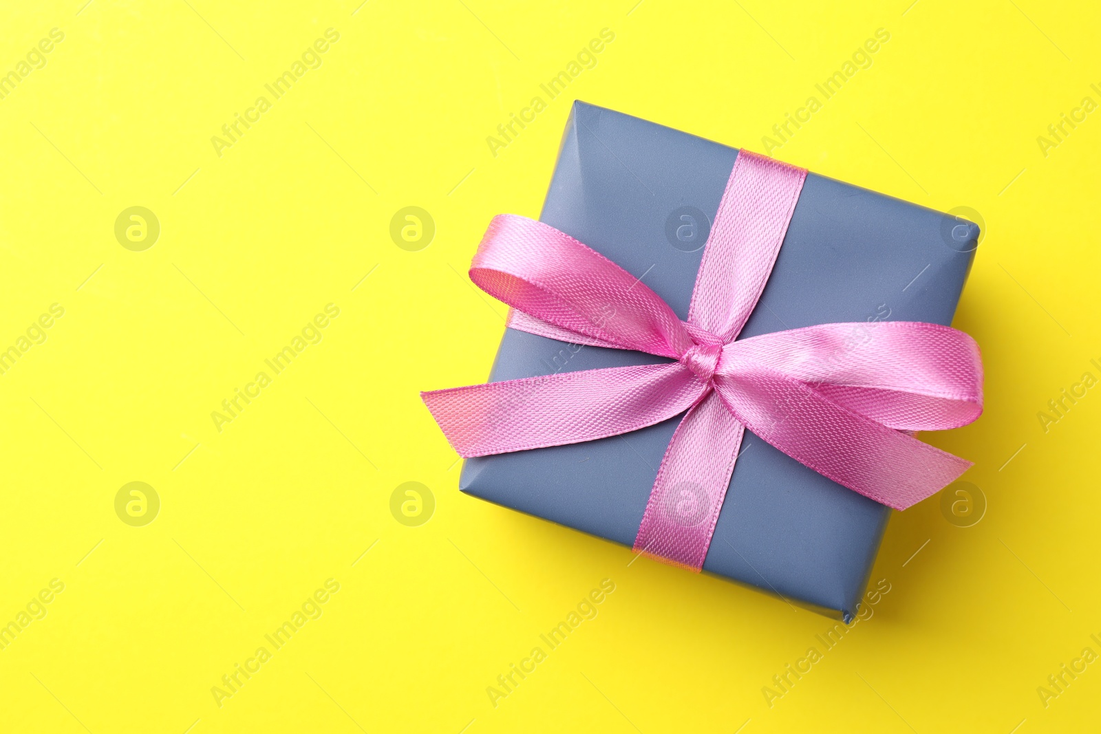 Photo of Gift box with pink bow on yellow background, top view. Space for text