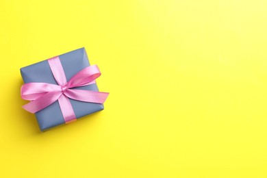 Photo of Gift box with pink bow on yellow background, top view. Space for text