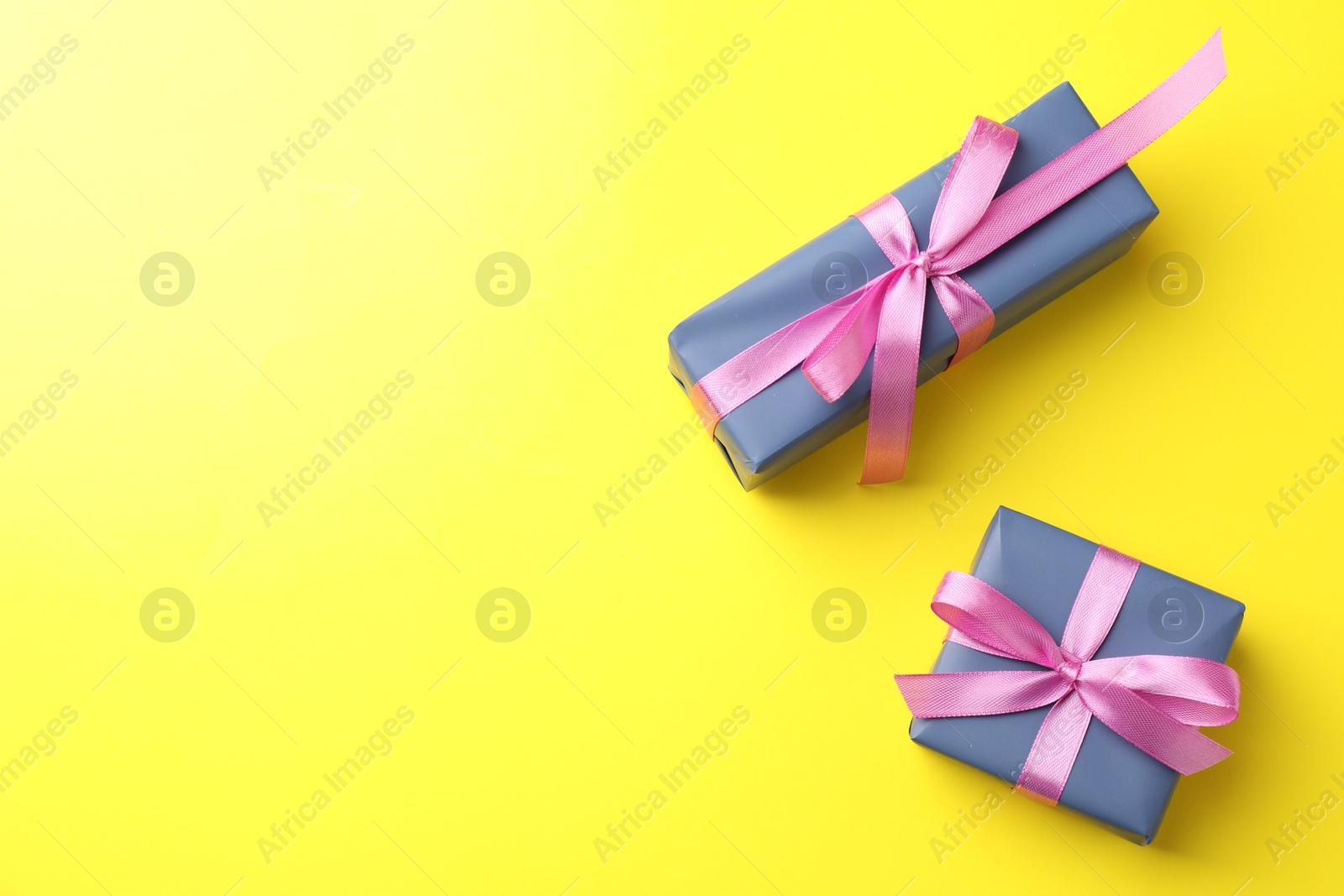 Photo of Gift boxes with pink bows on yellow background, top view. Space for text