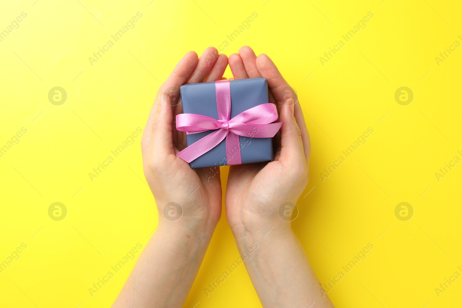 Photo of Woman holding gift box with pink bow on yellow background, top view