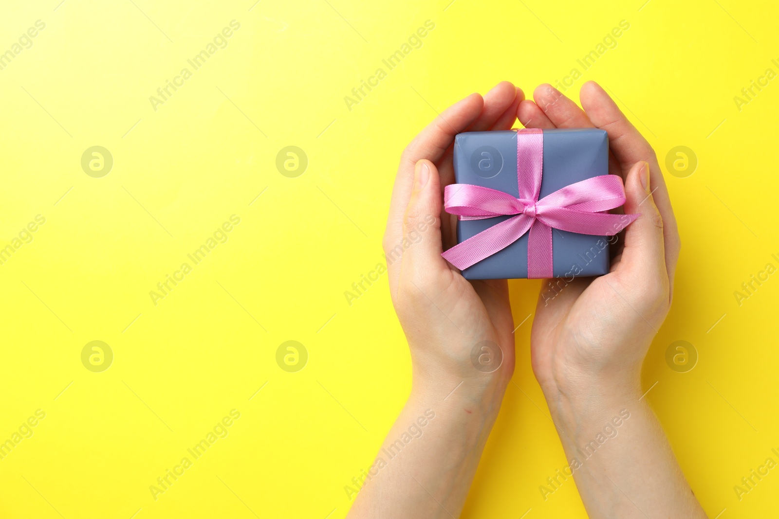 Photo of Woman with gift box on yellow background, top view. Space for text