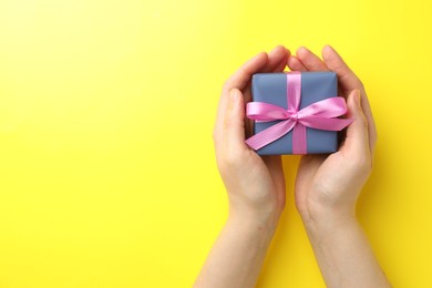 Woman with gift box on yellow background, top view. Space for text