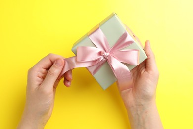 Photo of Woman holding gift box with pink bow on yellow background, top view