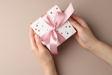 Photo of Woman holding gift box with pink bow on beige background, top view