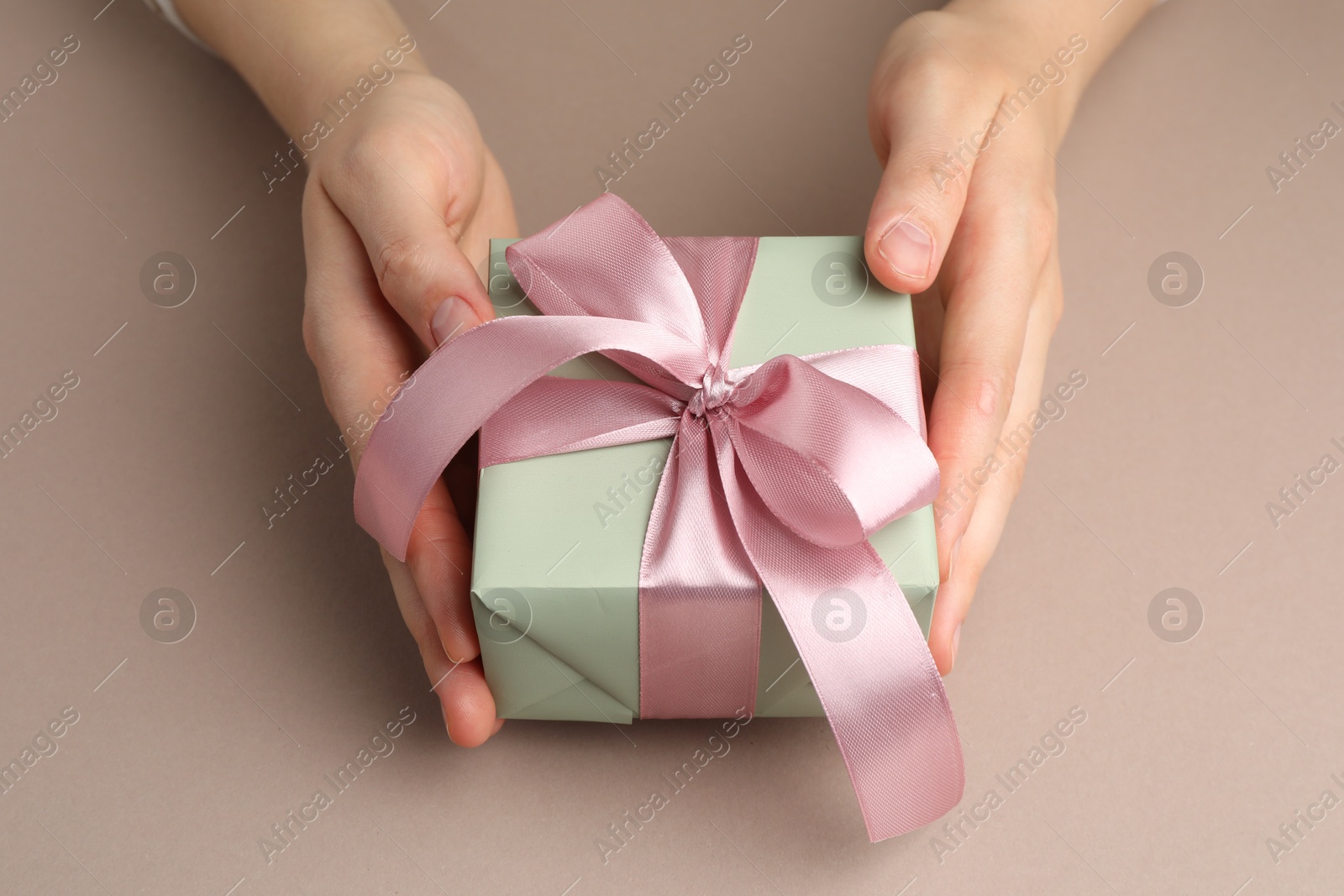 Photo of Woman holding gift box with pink bow on beige background, closeup