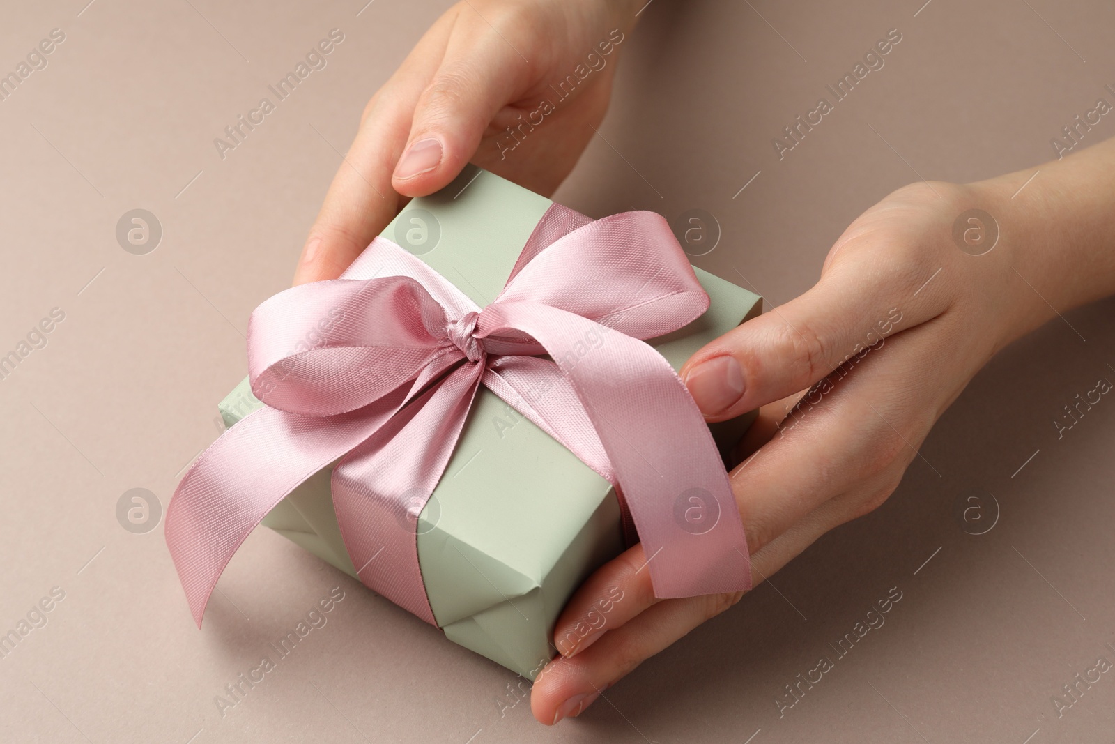 Photo of Woman holding gift box with pink bow on beige background, closeup