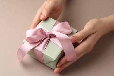 Photo of Woman holding gift box with pink bow on beige background, closeup