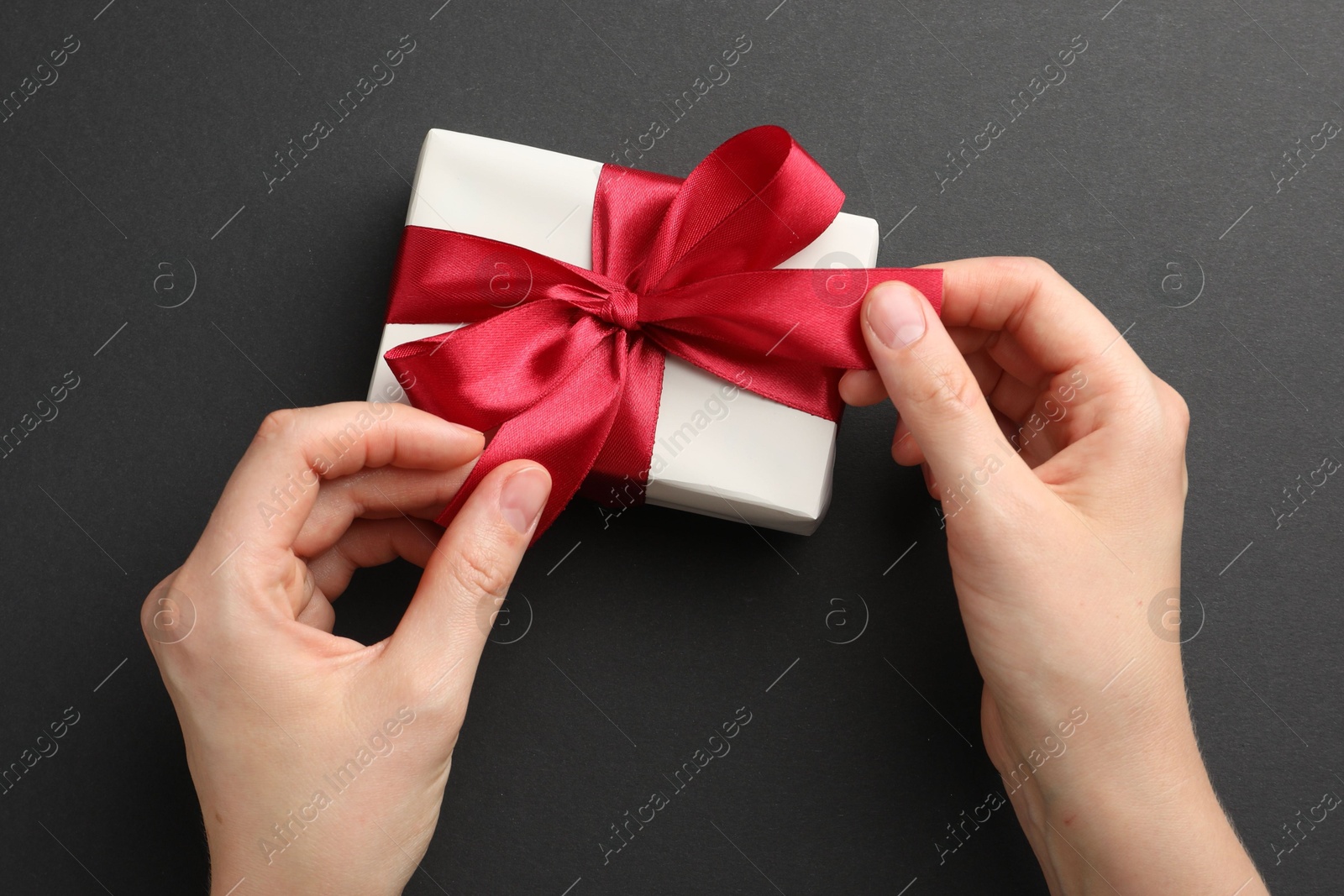 Photo of Woman opening gift box on black background, top view