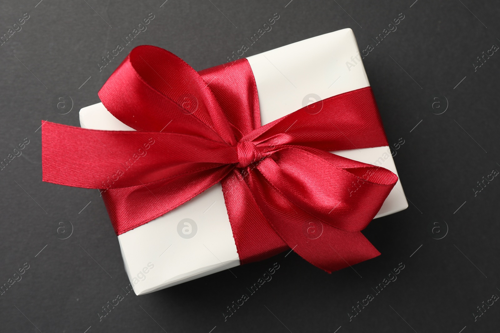 Photo of Gift box with red bow on black background, top view