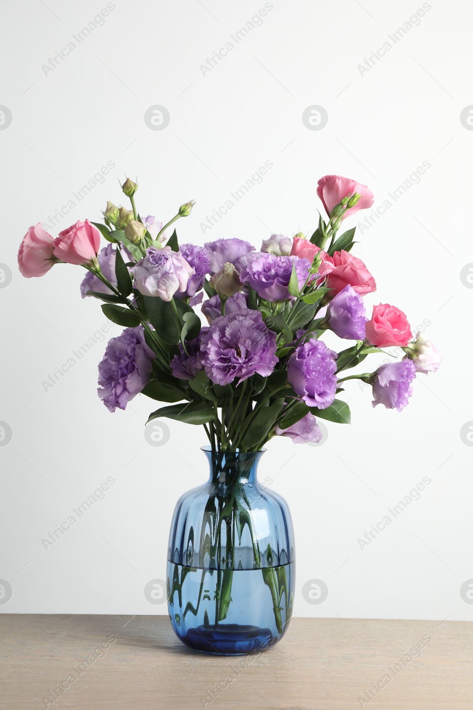 Photo of Vase with beautiful eustoma flowers on wooden table