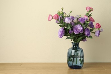 Vase with beautiful eustoma flowers on wooden table, space for text