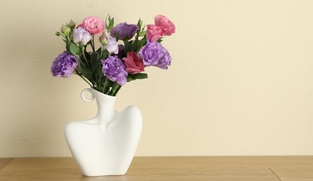 Vase with beautiful eustoma flowers on wooden table, space for text