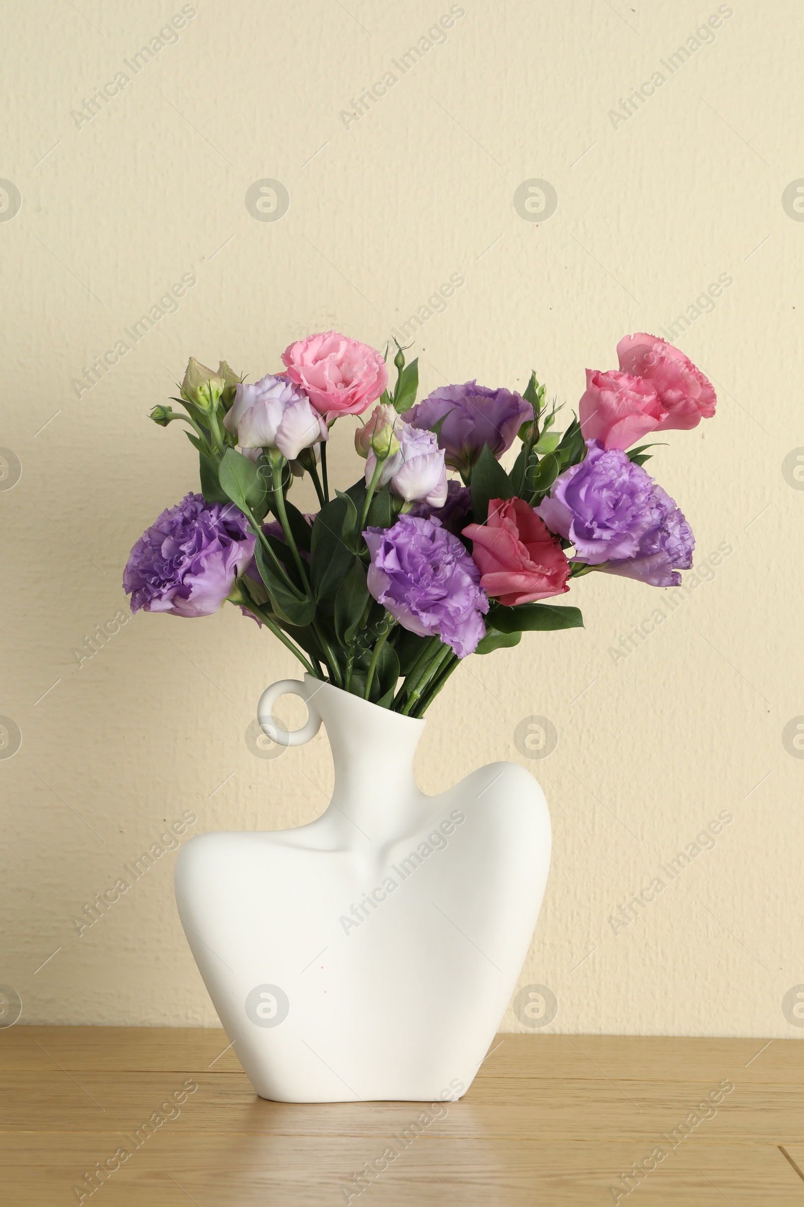 Photo of Vase with beautiful eustoma flowers on wooden table